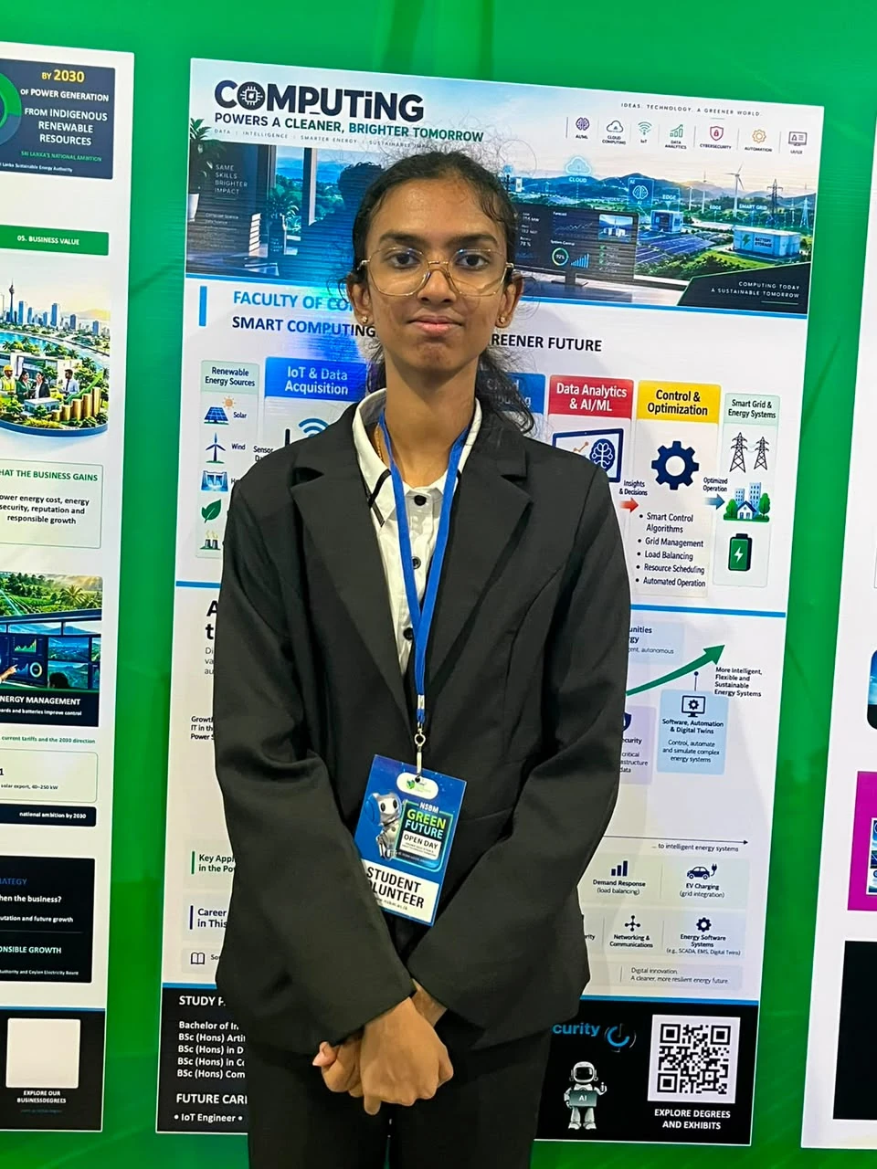 A club member wearing glasses and an Open Day volunteer lanyard in front of the computing billboard